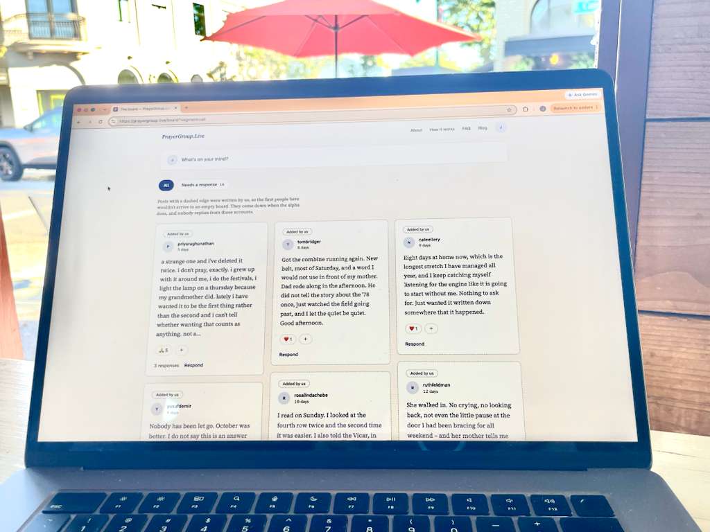 A laptop open on an outdoor table, showing the PrayerGroup.Live board with members’ posts side by side.